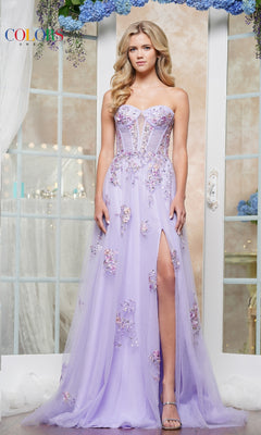 A woman poses indoors in front of floral-adorned French doors, wearing the Strapless Long Prom Ball Gown: Colors Dress 3575—a lilac gown with floral appliqué details and a thigh-high slit.