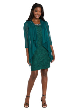 A woman stands smiling in the R&M Richards 3594 Short Semi-Formal Jacket Dress—teal, knee-length with lace and a sheer draped layer—styled with black strappy heels, ideal for chic cocktail or semi-formal events.