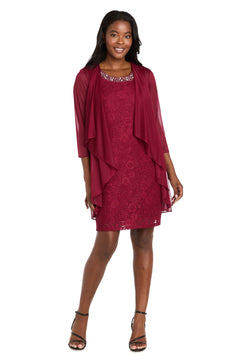 A woman stands smiling in the elegant R&M Richards 3594, a short semi-formal jacket dress in burgundy lace with a matching sheer draped jacket and black strappy heels.