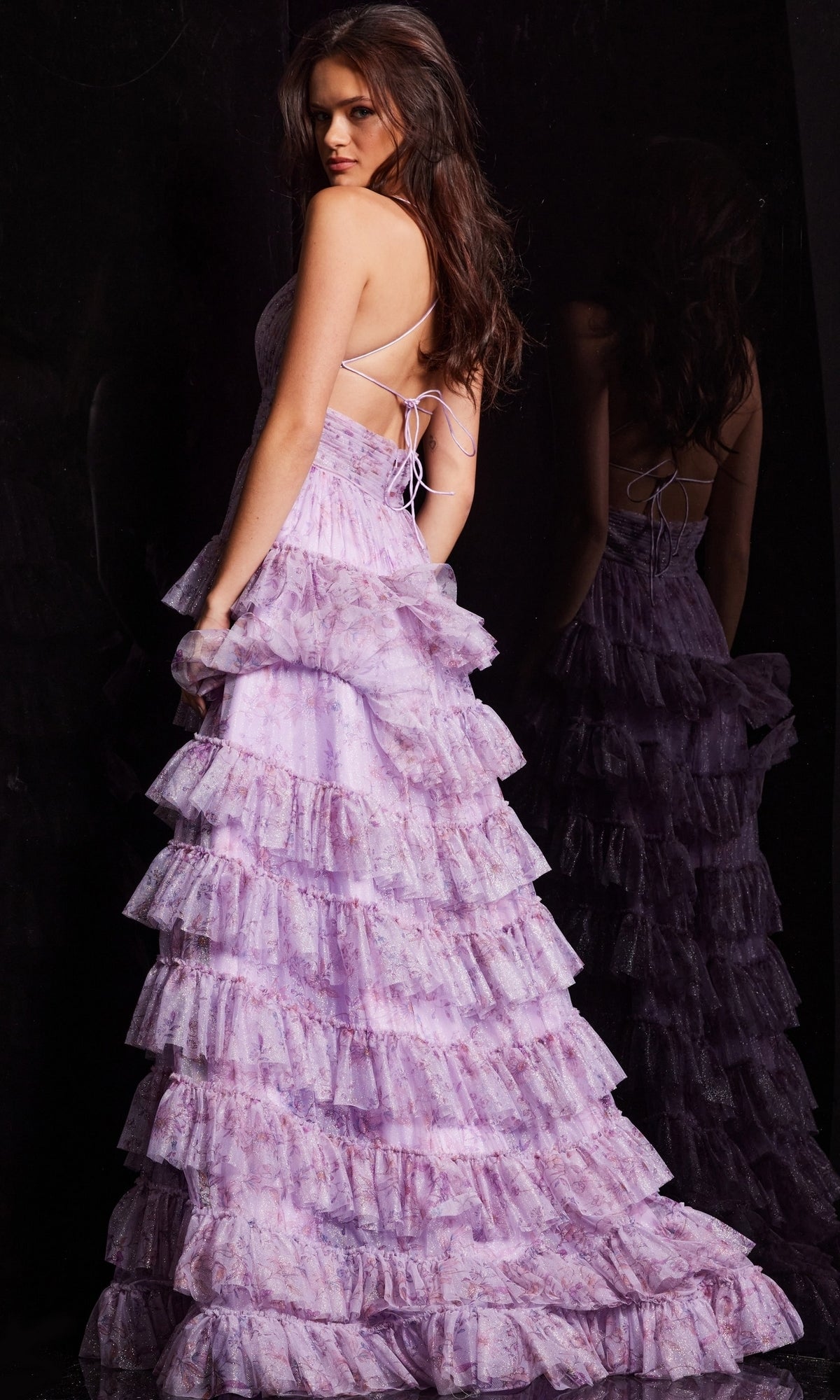 A woman stands in profile, posing gracefully in front of a mirror while wearing the Jovani 36571 Long Print Ruffled A-Line Prom Dress with thin straps.