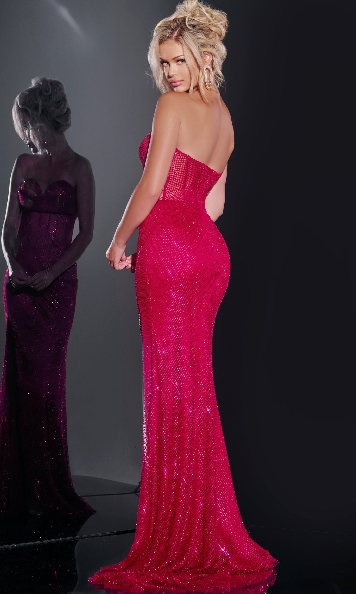 A woman in the Jovani 36684 long prom dress, featuring a strapless sweetheart neckline and bright pink sequins, stands facing away as her shimmering reflection appears in the mirror beside her.