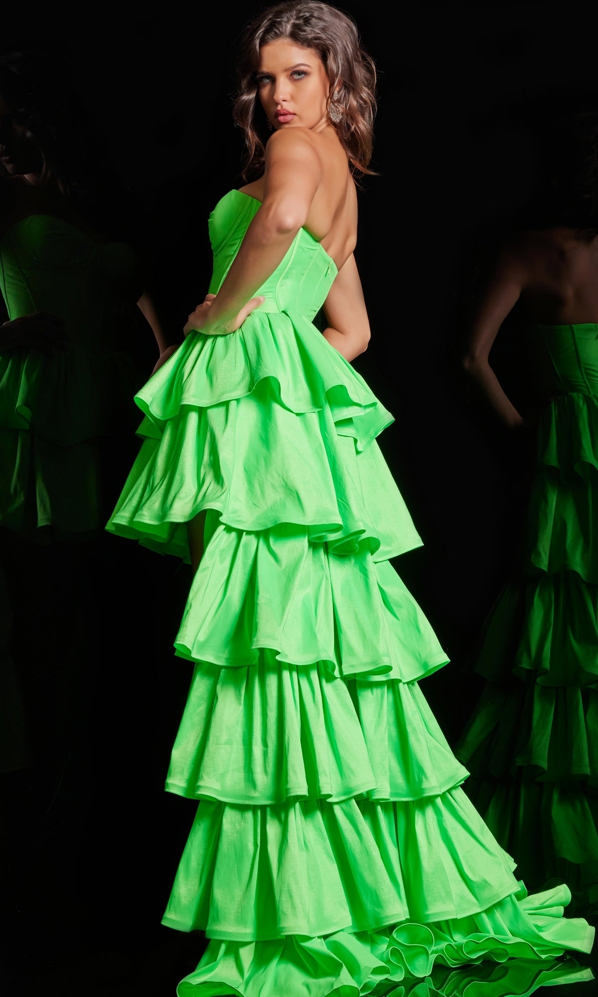 A woman poses in the High Low Ruffled Prom Dress 36983 by Jovani, featuring a strapless sweetheart neckline and bright neon green layered ruffles, set against a striking black background.