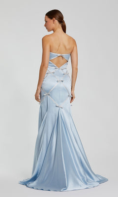 A woman models the strapless Mac Duggal 37000 long blue formal dress, featuring silver embellishments, diamond-shaped cutouts, and an open back, all highlighting this elegant occasion gown.