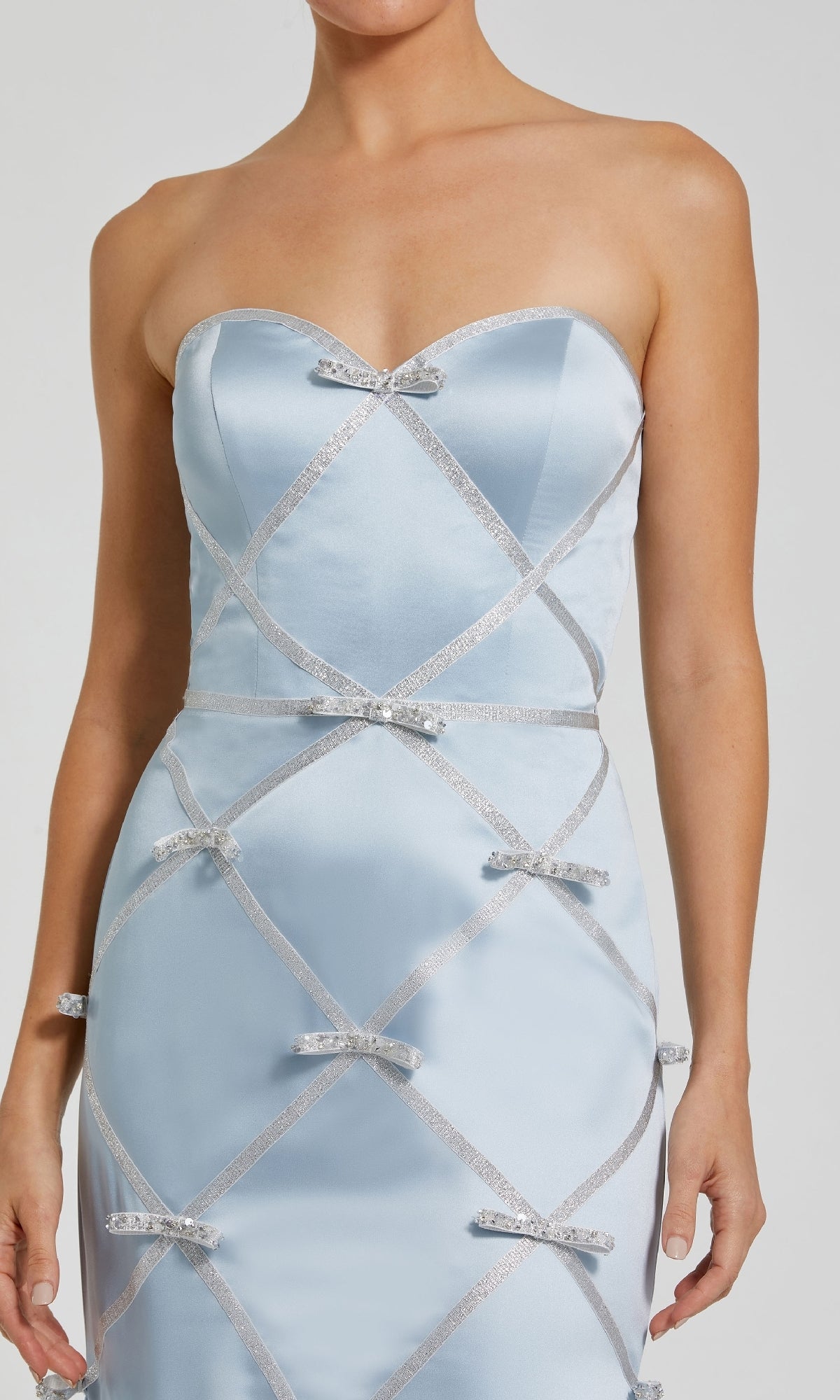 A woman wears the Mac Duggal 37000, a strapless long blue formal dress featuring silver ribbon crisscross patterns and small silver bows for an elegant evening look.