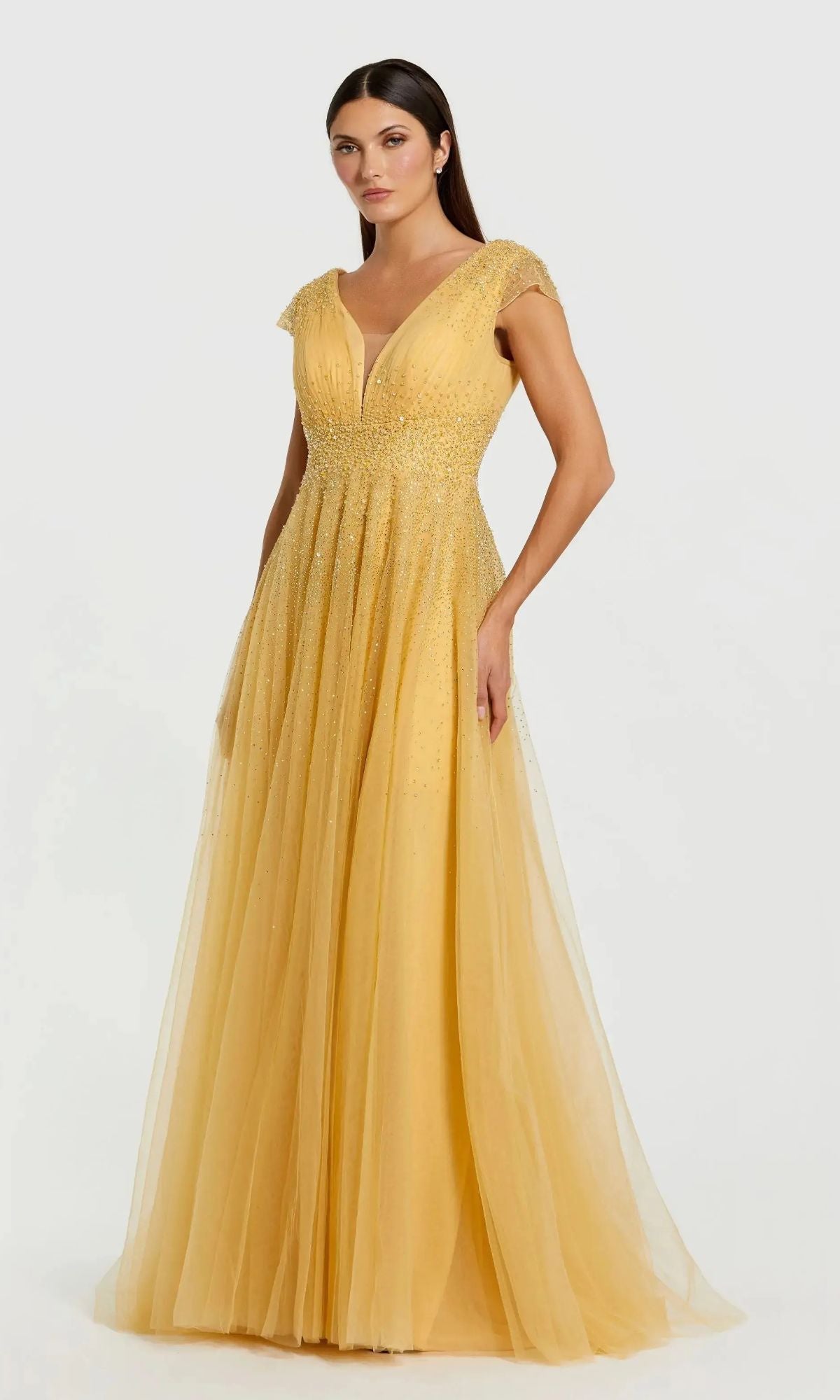 Woman in the gold Mac Duggal 37018 long formal dress featuring cap sleeves, a deep V neckline, and sparkling embellishments, standing against a plain light background.