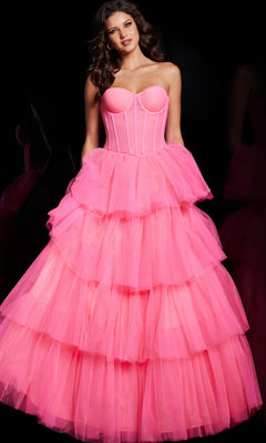 A woman stands against a black background wearing the Jovani 37062 Strapless Long Ruffle Prom Ball Gown in hot pink with a corset-style bodice and tiered tulle skirt.