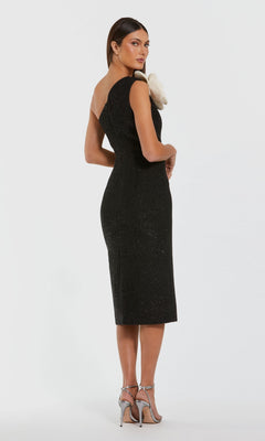 A woman models the Mac Duggal 37066 Midi Wedding Guest Dress, a black one-shoulder, knee-length piece with a subtle 3D floral accent and metallic heels, posed slightly away from the camera against a white background.