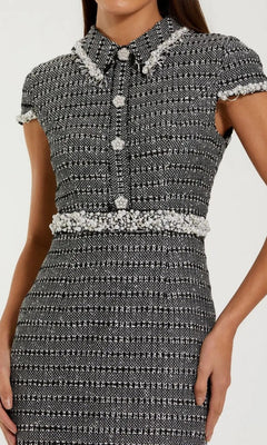 A woman in the Mac Duggal 37070 midi semi-formal dress, made from black and white boucle fabric and adorned with pearl trim and elegant pearl buttons.