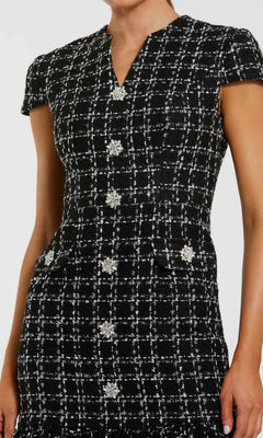 A woman wears the Mac Duggal 37071 Semi-Formal Midi Day Dress, featuring short sleeves, black and white plaid, embellished buttons, and decorative flap pockets; shown from shoulders to above the knees.