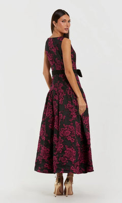 Woman wearing the Mac Duggal 37091 Floral Drop-Waist Party Dress—sleeveless, black with a pink floral pattern—paired with metallic heels, standing and glancing over her shoulder.