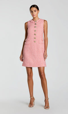 A woman poses against a plain light background, wearing the Mac Duggal 37136 Short Party Dress—a pink sleeveless mini dress in boucle fabric featuring gold buttons and two front pockets—styled with beige high-heeled sandals for a chic look.