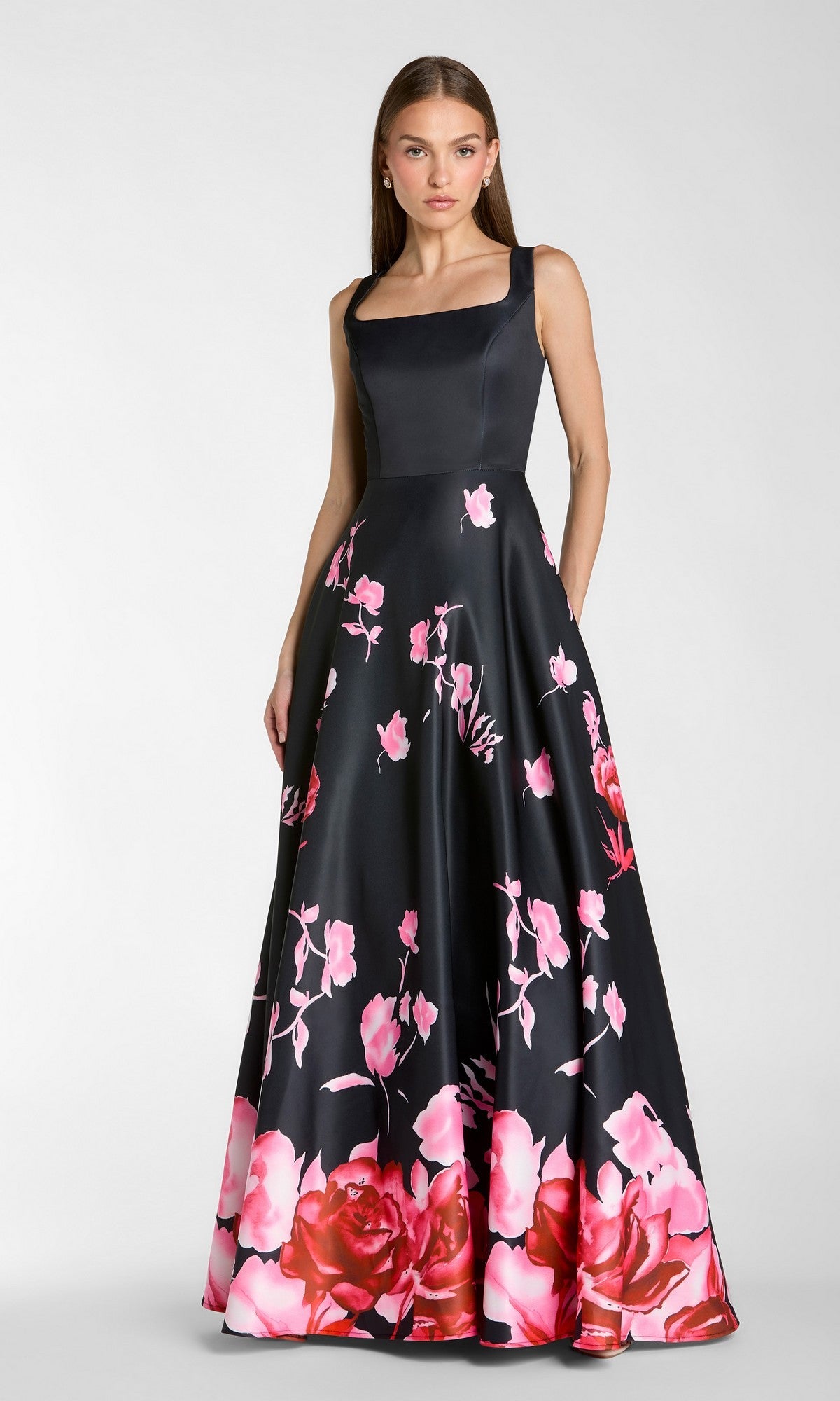 A woman stands against a plain background wearing the Mac Duggal 37149 long formal dress in Black Multi—this sleeveless, floor-length gown features a square neckline and a vibrant pink floral print on the skirt.