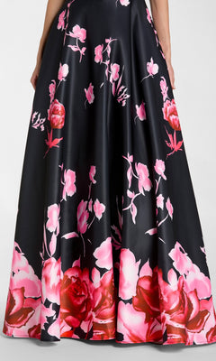 A person wearing the Long Formal Dress: Mac Duggal 37149, a black satin ballgown with pink and red floral patterns, stands with their hands near the skirt’s side seams.