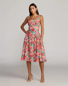 A woman wearing the "Floral Midi Wedding Guest Dress: Mac Duggal 37155" in Pink Multi, a sleeveless crepe midi dress with a square neckline and a colorful floral pattern, stands with one hand on her hip against a plain background.