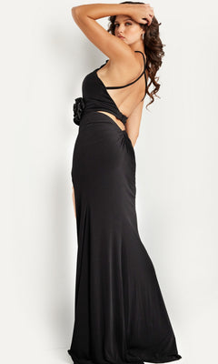 A woman models the Long Prom Dress 37164 by Jovani, featuring a black, open back design with side cutouts, standing sideways and glancing over her shoulder.