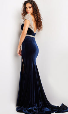 A woman in the Long Prom Dress 37246 by Jovani, featuring navy blue crystal-embellished velvet, beaded cap sleeves, and an open back, stands against a light background, looking over her shoulder.