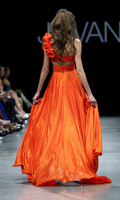 A model is seen from behind wearing the Jovani 37254 one-shoulder long metallic prom gown on the runway.