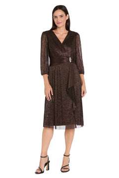 A woman models the R&M Richards 3741 Metallic Knee-Length Party Dress with long sleeves, V-neckline, pleated skirt, and black high-heeled sandals, standing against a white background.
