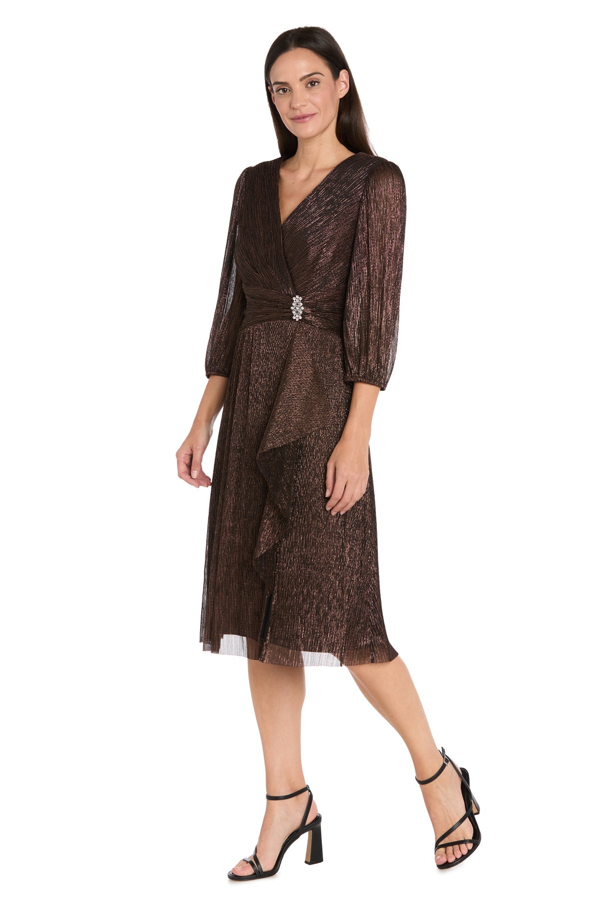 Woman wears the R&M Richards 3741 Metallic Knee-Length Party Dress, featuring three-quarter sleeves, a v-neckline, and waist ruffles in shimmery brown fabric—perfect for any semi-formal event. She pairs it with black strappy heels.