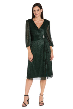 Woman in the R&M Richards 3741 Metallic Knee-Length Party Dress, featuring sheer long sleeves, V-neckline, gathered waist with jeweled brooch, and black heeled sandals, standing against a white background.