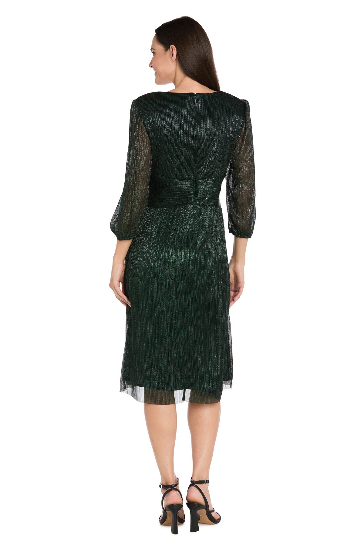 A woman stands facing away, wearing the R&M Richards 3741 Metallic Knee-Length Party Dress with sheer long sleeves and black high-heeled sandals.