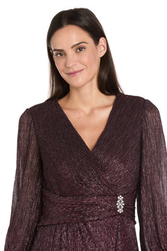 Woman with long brown hair wears the R&M Richards 3741 Metallic Knee-Length Party Dress, featuring textured purple fabric and a decorative waist brooch, standing against a white background.