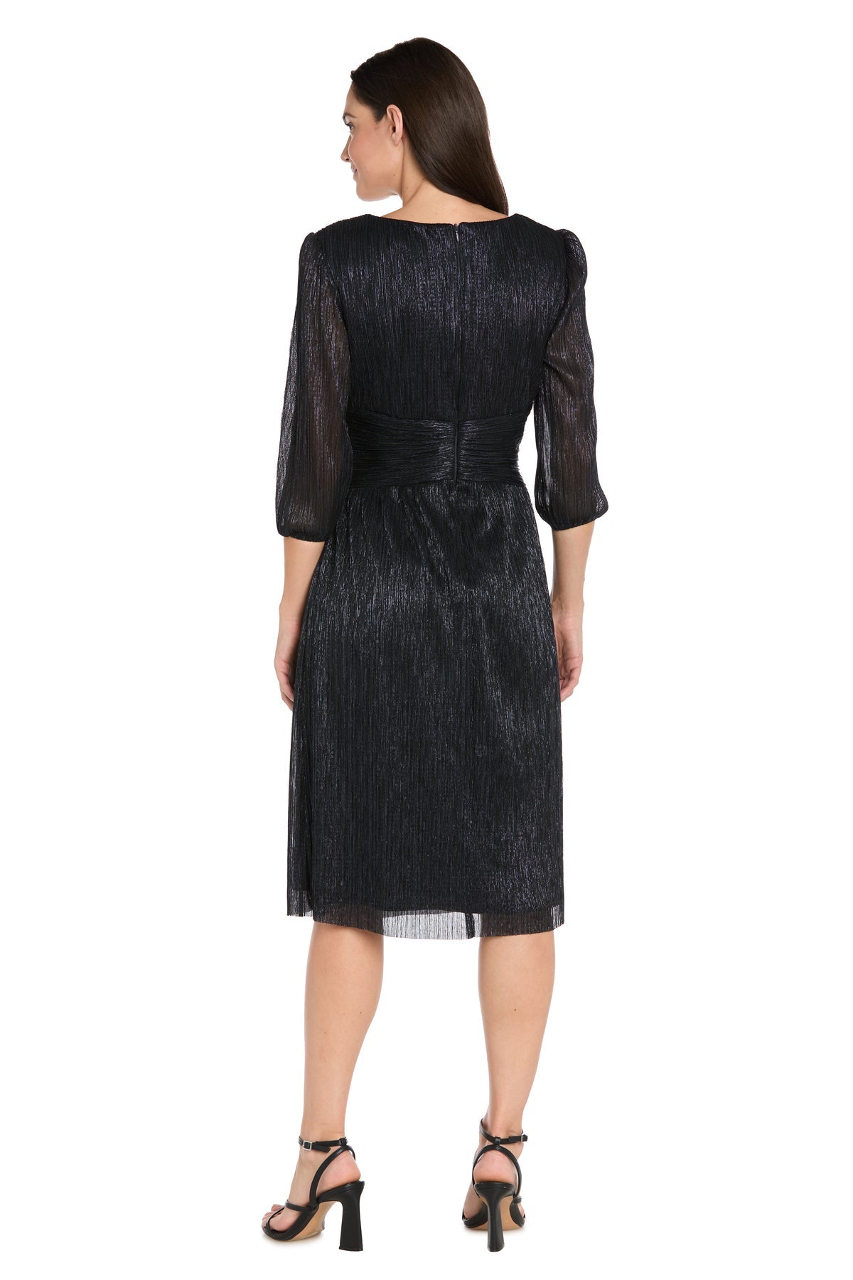 A woman faces away, wearing the R&M Richards 3741 Metallic Knee-Length Party Dress with three-quarter sleeves and shimmery black fabric, paired with black heeled sandals.