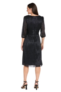 A woman stands facing away in the R&M Richards 3741 Metallic Knee-Length Party Dress with three-quarter sleeves and black heeled sandals. The shimmery black fabric enhances the elegance of this semi-formal look against a white background.