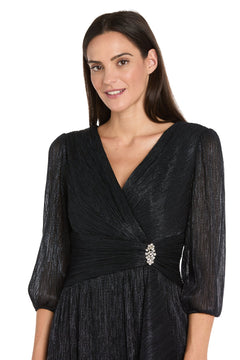 A woman poses against a plain background in the R&M Richards 3741 Metallic Knee-Length Party Dress, featuring three-quarter sleeves and a jeweled brooch at the waist.