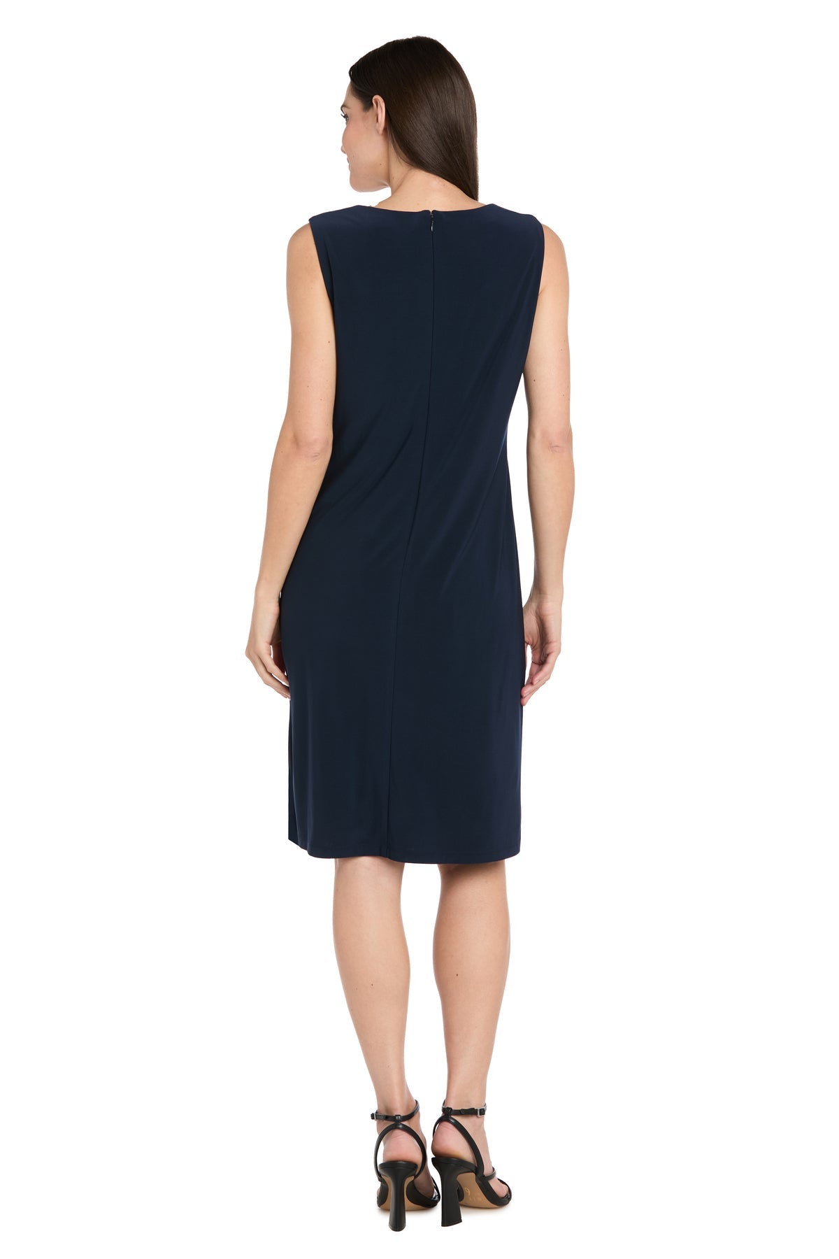 A woman in the R&M Richards 3742 Short Navy Jacket Party Dress and black high-heeled sandals stands facing away from the camera against a white background.