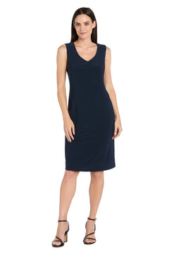 A woman models the R&M Richards 3742 Short Navy Jacket Party Dress, a sleeveless knee-length party dress with a V-neckline, paired with black strappy heels, standing against a white background.