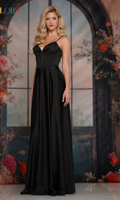A woman in the Colors Dress 3743, a long satin corset prom dress, stands before a floral backdrop with a large arched window, her elegant evening gown shimmering in the light.