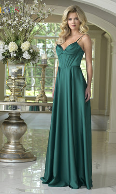 A woman in the Long Satin Corset Prom Dress: Colors Dress 3743 in deep green, featuring spaghetti straps, stands indoors beside a round table decorated with floral arrangements.