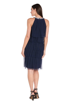 A woman stands with her back turned, wearing the R&M Richards 3744 short navy blue cocktail dress featuring tiered chiffon ruffles and black heeled sandals against a white background.