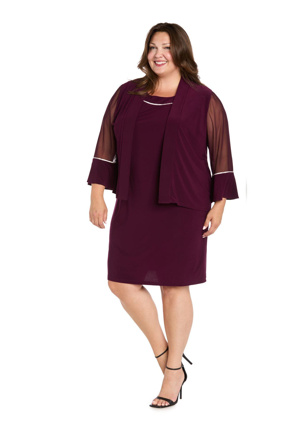 A woman wearing the R&M Richards 3747W Short Plus-Size Jacket Party Dress—a knee-length, plum design with sheer sleeves and a matching shawl—stands smiling against a white background.