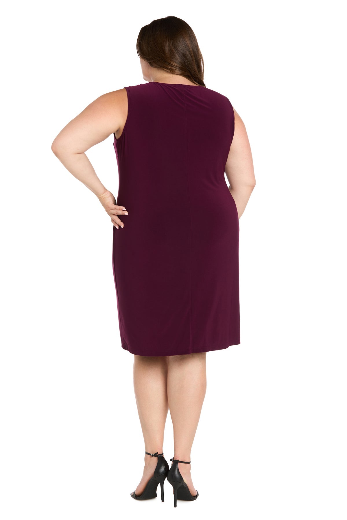 A woman in the R&M Richards 3747W Short Plus-Size Jacket Party Dress—sleeveless, knee-length, burgundy—paired with black heeled sandals stands facing away, one hand on her hip.