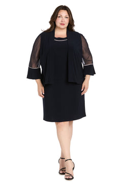 A woman stands facing forward against a white background wearing the R&M Richards 3747W Short Plus-Size Jacket Party Dress in black with sheer sleeves, black open-toe heels, and a matching jacket.