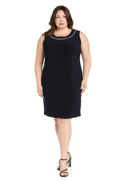 A woman wearing the R&M Richards 3747W Short Plus-Size Jacket Party Dress—a sleeveless, knee-length black dress—paired with black heeled sandals, stands against a white background.