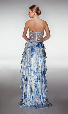 Woman wearing the Long Prom Dress: Aerie Couture 374, featuring blue and white florals, a sheer corset bodice, and a tiered ruffle A-line skirt, stands with her back to the camera against a plain backdrop.
