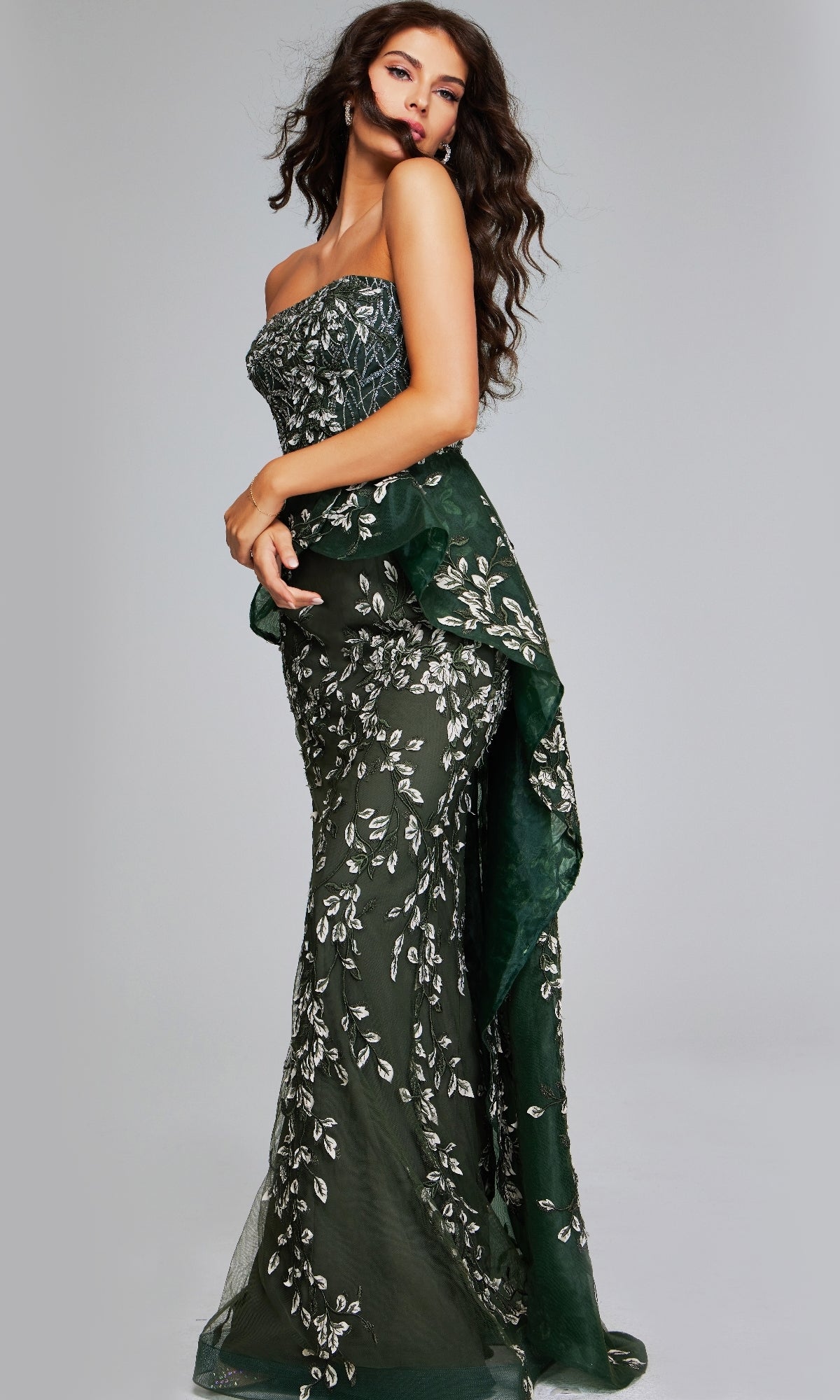 A woman models the Jovani 37599 long dark green formal dress, featuring silver floral embroidery and ruffle details, against a plain light background.
