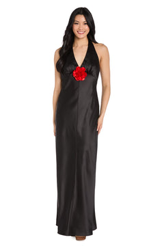 A woman in the R&M Richards 3773, a long black satin halter formal dress with a floor-length silhouette and large red flower detail at the center front—an elegant choice for any black-tie event.