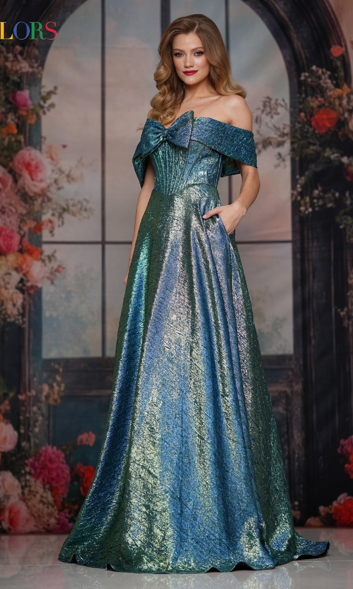 A woman stands in front of a floral and window backdrop, wearing the Off-Shoulder Corset Prom Gown Colors Dress 3792 in teal green, featuring a shimmering finish, structured bodice, and full skirt.