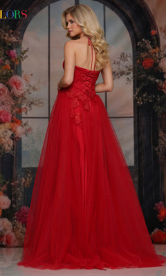 Wearing the Colors Dress 3796, a woman stands before a floral arched window backdrop. The long prom dress features a lace-up back, 3D floral appliques, and an elegant A-line tulle skirt as she looks over her shoulder.