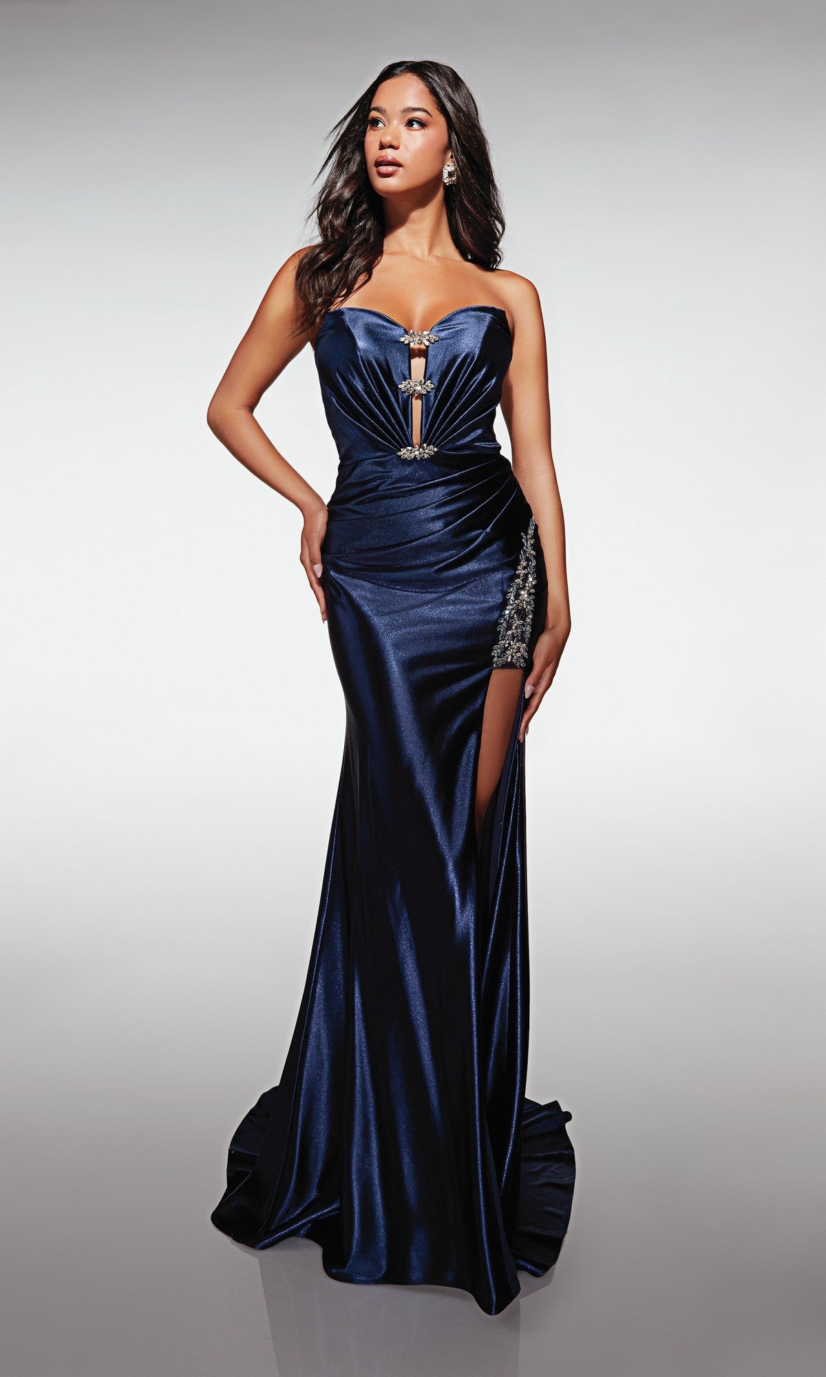 A woman stands against a plain light background in the Aerie Couture 379 long prom dress, a midnight strapless satin gown with a fitted silhouette, floor-length hem, thigh-high slit, and jeweled details.
