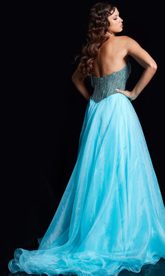 A woman with long wavy hair stands with her back turned against a black background, wearing the Jovani 38179 long prom dress featuring sparkling blue and silver details and a beaded strapless corset bodice.
