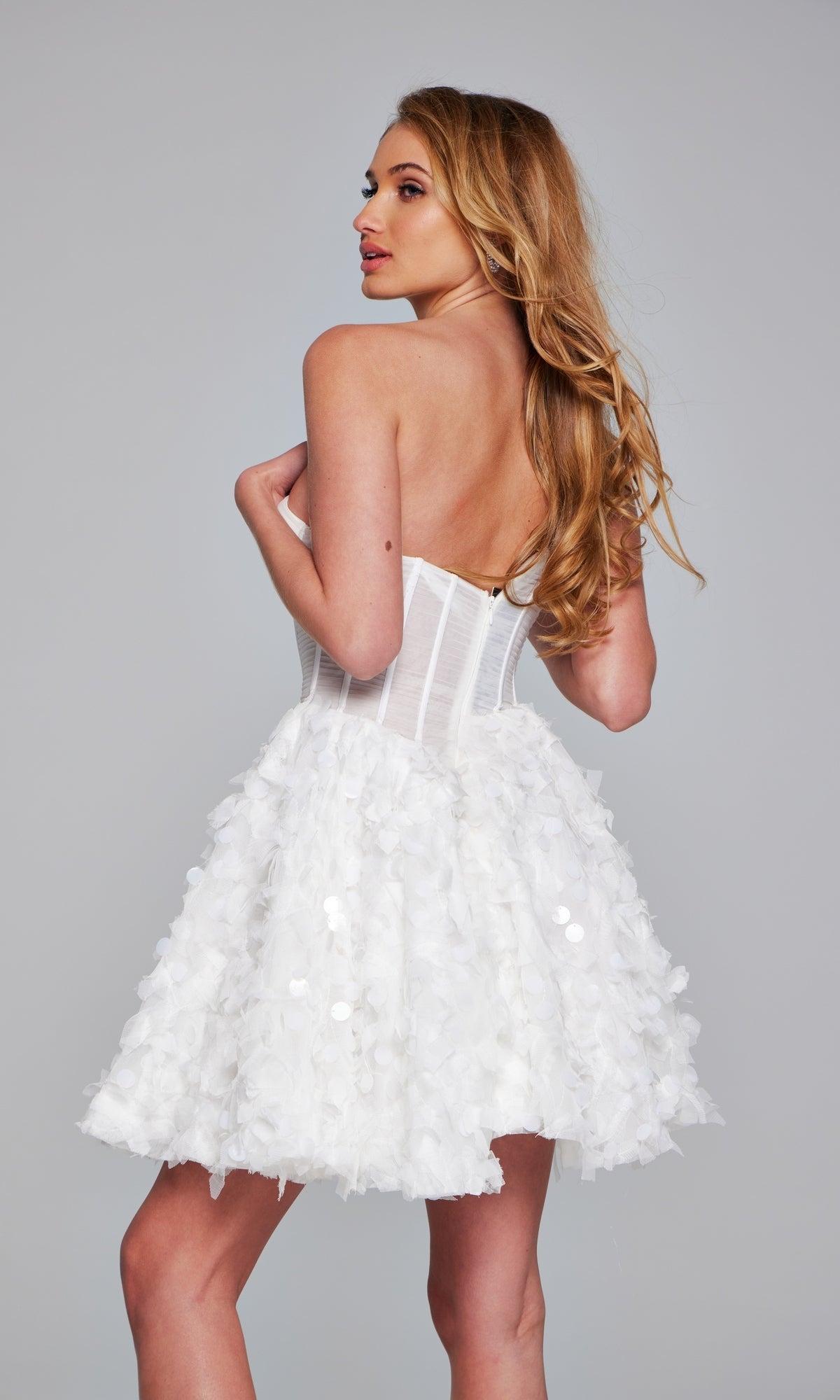 A woman with long blonde hair poses against a gray background in the Jovani Strapless Short White Hoco Dress 38248, featuring a fitted bodice and textured flared skirt—ideal as a short white homecoming dress.