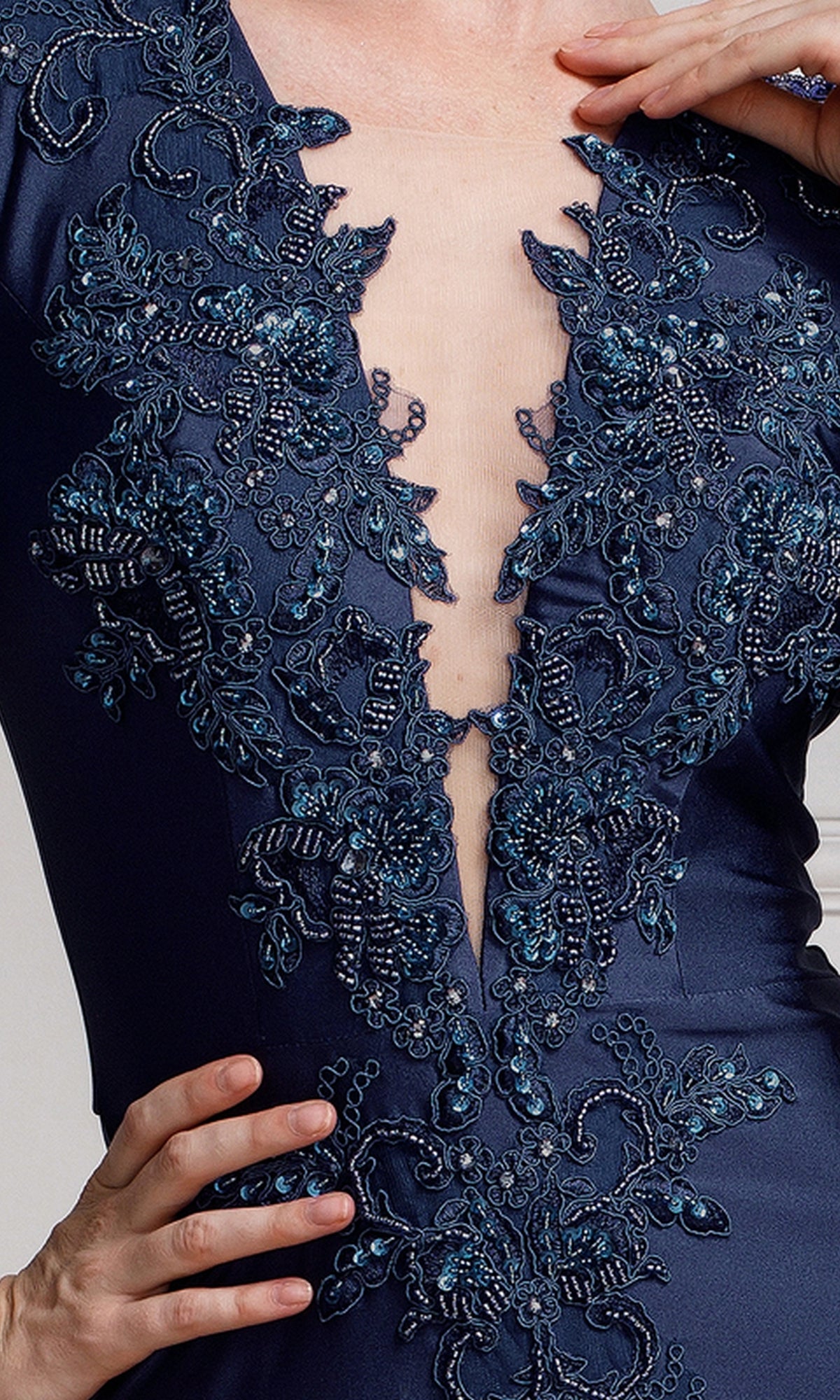 Close-up of a person wearing Long-Sleeve Plunging V-Neck Long Formal Dress 382 in navy blue, featuring intricate beaded embroidery and a deep V neckline. Their hand is resting on their hip.