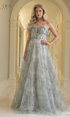A woman stands in a hallway wearing the Colors Dress 3831, a long prom dress with 3D floral appliques, a sheer bodice, and a deep V neckline.
