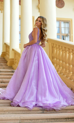 A woman in the Ava Presley 38342 Deep V-Neck Long Prom Ball Gown poses on marble stairs framed by cream columns, glancing over her shoulder. Her sleeveless lavender gown features a fitted bodice and a voluminous skirt.