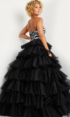 A woman wears the Jovani Black White Long Ruffled Prom Dress 38360, featuring a strapless zebra-pattern bodice and a voluminous tiered black ruffled skirt, as she stands looking over her shoulder.